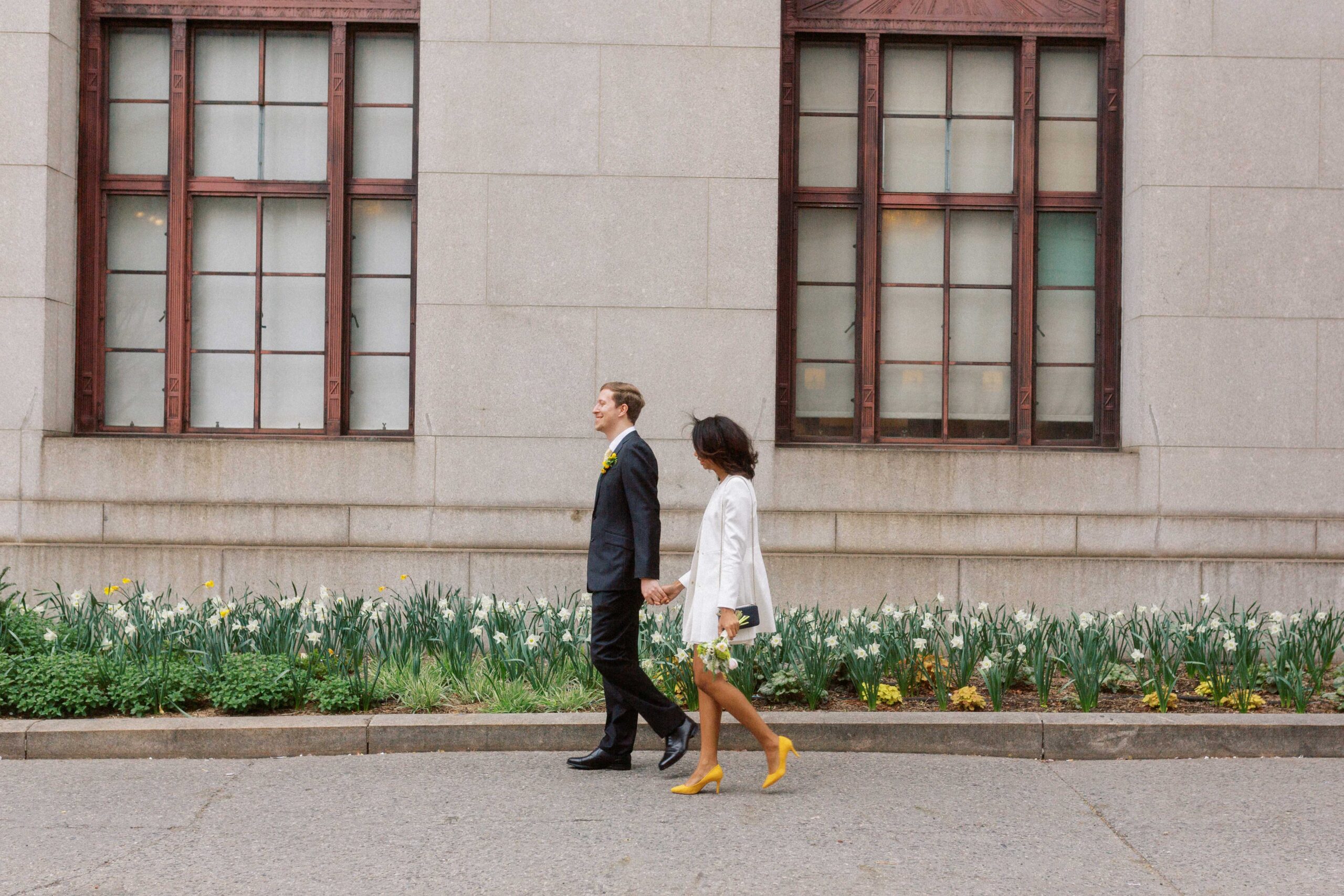 nyc city hall wedding photographer elopement couple outside of nyc marriage bureau in manhattan walking along garden of yellow daffodils